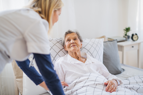Bettlägige Seniorin wird von Krankenpflegerin versorgt
