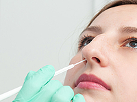 Ein Mediziner nimmt einen Nasenabstrich einer potentiell erkrankten jungen FrauNasenabstrich einer jungen Patienten durch medizinisches Personal