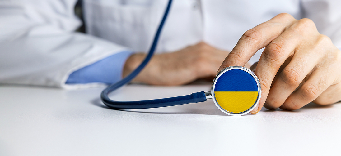 Arzt hält Stethoskop mit symbolischer Einfärbung der Ukraine-Nationalfarben