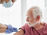 Ein Senior wird von einem Arzt in Schutzkleidung geimpft