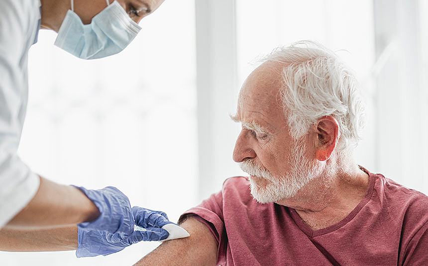 Ein Senior wird von einem Arzt in Schutzkleidung geimpft